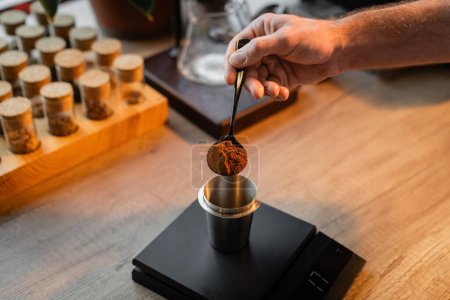 Foto de Vista recortada de barista vertiendo café en vaso de precipitados en balanza electrónica y encimera en cafetería - Imagen libre de derechos