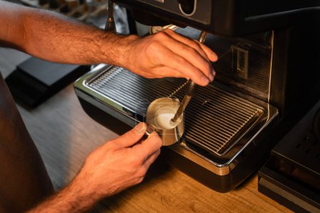 high angle view of barista frothing milk on coffee machine while working in coffee shop