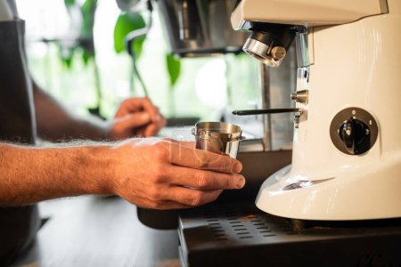 Foto de Vista recortada de barista sosteniendo vaso de precipitados cerca de molinillo de café mientras trabajaba en la cafetería - Imagen libre de derechos