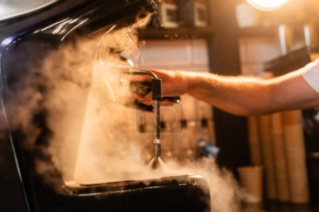 Foto de Vista recortada de barista en delantal usando cafetera cerca de vapor e iluminación en cafetería - Imagen libre de derechos