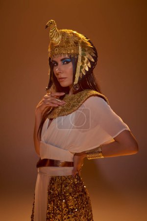 Photo for Elegant woman in egyptian look and headdress looking at camera on brown background - Royalty Free Image