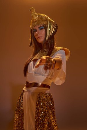 Frau in ägyptischer Kleidung zeigt mit dem Finger auf Kamera und steht auf braunem Hintergrund mit Licht