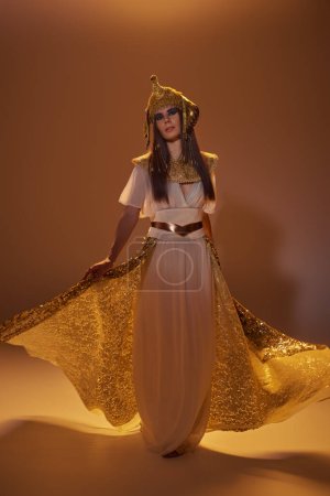 Volle Länge der Frau in ägyptischer Kleidung mit elegantem Rock, während sie auf braunem Hintergrund steht
