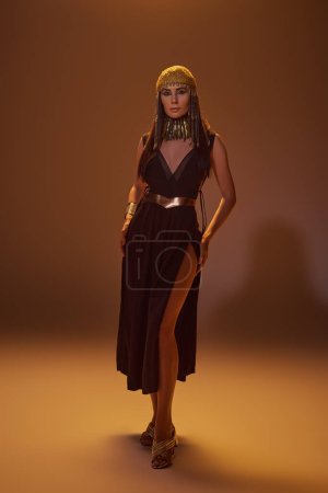 Photo for Full length of elegant woman in egyptian look and headdress standing and posing on brown background - Royalty Free Image