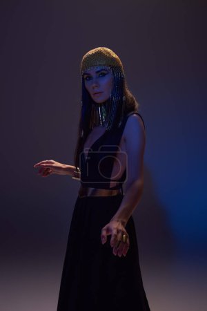Brünette Frau im traditionellen ägyptischen Look blickt in die Kamera auf braunem Hintergrund mit blauem Licht
