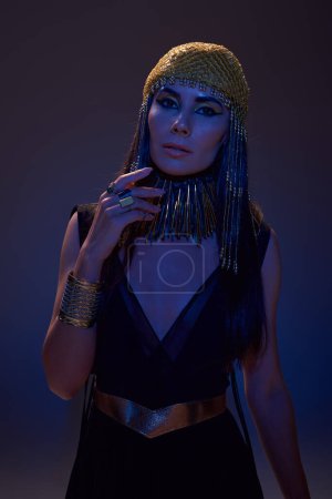 Porträt einer stilvollen Frau in ägyptischem Kostüm, die in die Kamera blickt, in blauem Licht auf braunem Hintergrund