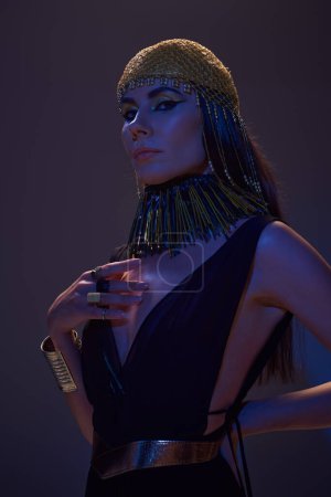 Retrato de mujer hermosa en traje egipcio posando y mirando a la cámara en marrón con luz azul