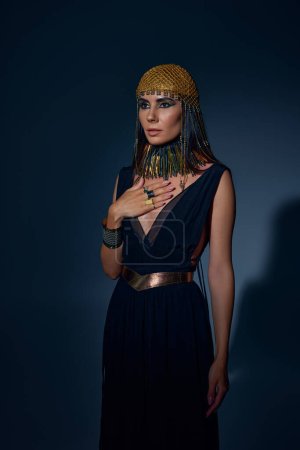 Mujer elegante en tocado egipcio y collar posando sobre fondo azul