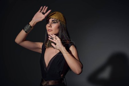 Schöne Frau in ägyptischem Kleid und Halskette posiert auf schwarzem Hintergrund mit Schatten