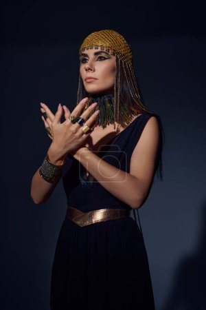 Modische Frau in ägyptischem Kleid und Kopfbedeckung posiert auf blauem Hintergrund