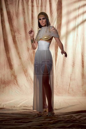 Trendiges Modell in ägyptischer Kleidung und Perlentop posiert auf abstraktem Hintergrund