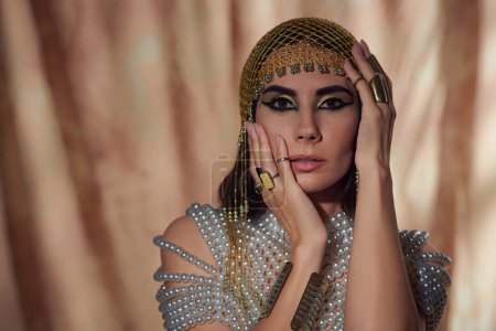 Téléchargez les photos : Portrait de femme en coiffure égyptienne et haut perlé touchant sur fond abstrait - en image libre de droit