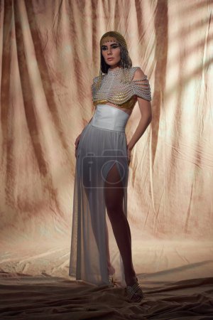 Volle Länge der eleganten brünetten Frau in ägyptischer Kleidung posiert auf abstraktem Hintergrund