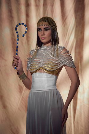 Elegante mujer en aspecto egipcio y top de perlas sosteniendo ladrones tradicionales sobre fondo abstracto