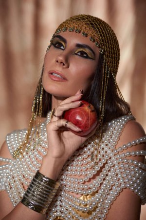 Porträt einer Frau in eleganter ägyptischer Kleidung mit reifem Granatapfel auf abstraktem Hintergrund