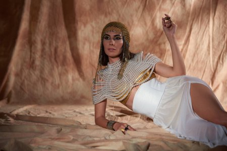 Elegante Frau in ägyptischem Kostüm und Perlenoberteil auf abstraktem Hintergrund mit Sonnenlicht