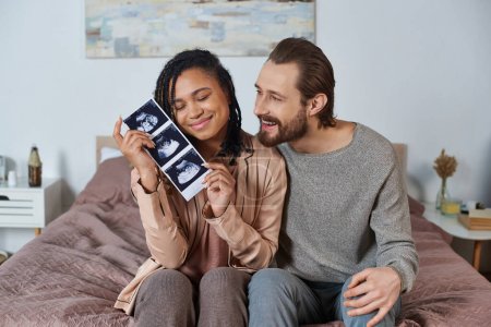 happy interracial husband and wife, future parents, pregnant woman holding ultrasound scan