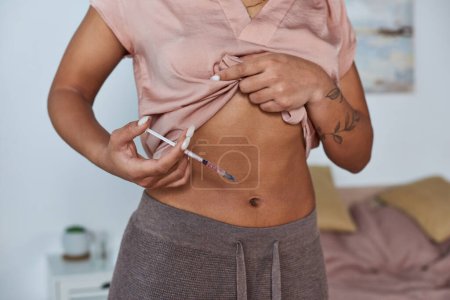 abgeschnittene Ansicht, afrikanisch-amerikanische Frau macht Hormonspritzen in Bauch, Tätowierung, Schwangerschaftskonzept