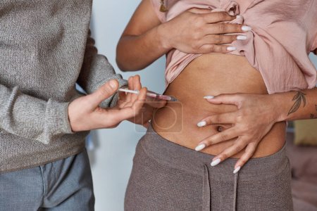 cropped man making hormonal injections in belly of african american wife, tattoo, fertility concept