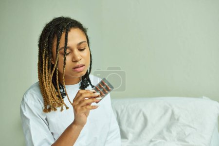 Foto de Mujer afroamericana en bata de hospital sosteniendo pastillas, sala privada, aborto espontáneo, paciente en clínica - Imagen libre de derechos