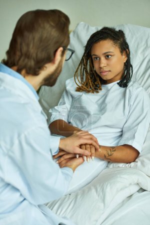 doctor en bata blanca cogido de la mano de la mujer afroamericana, reconfortante, sala privada, aborto espontáneo