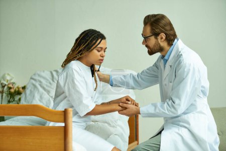 doctor masculino cogido de la mano de la mujer afroamericana, paciente reconfortante, sala privada, hospital