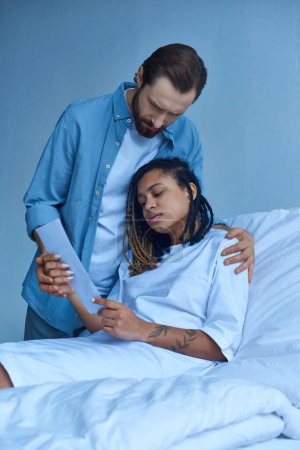 trauriger Mann steht neben afrikanisch-amerikanischer Frau, schaut Ultraschall, Krankenhaus, Fehlgeburtenkonzept