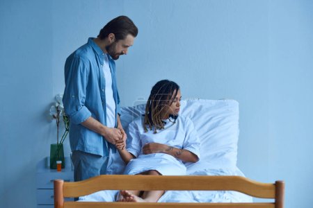 miscarriage concept, man holding hands of african american wife, comforting, hospital patient