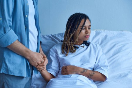 Fehlgeburtenkonzept, Mann hält Hand von depressiver afrikanisch-amerikanischer Frau, tröstet, Krankenhaus