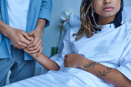 miscarriage concept, man holding hand of depressed african american wife, comforting, hospital, crop