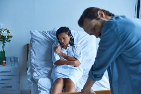 Fehlgeburtenkonzept, depressive Afroamerikanerin liegt neben Ehemann im Krankenhausbett, Trauer