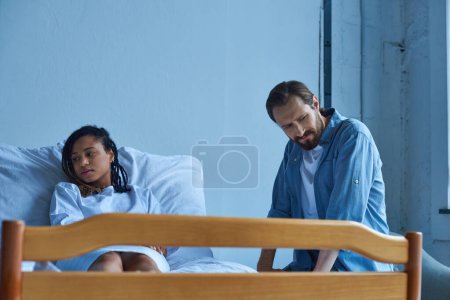 aborto espontáneo, hombre sentado cerca de la mujer afroamericana deprimida, dolor, cama de hospital, sala privada