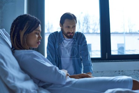 aborto espontáneo, hombre sentado cerca de la mujer afroamericana deprimida, desenfoque, cama de hospital, sala privada