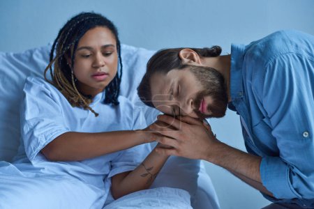 miscarriage concept, sad man grieving and holding hands of african american wife, hospital ward