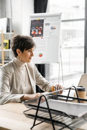 empresaria de mediana edad que trabaja en el ordenador portátil cerca del café para ir en la oficina, la confianza y la experiencia
