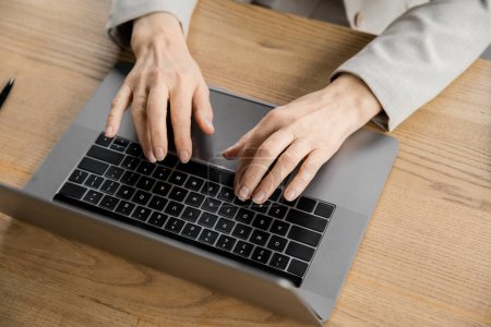 vista recortada de la mujer de negocios de mediana edad escribiendo en el ordenador portátil en la oficina moderna, vista superior