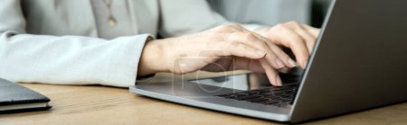 middle aged woman, executive manager, typing on laptop in contemporary office, cropped view, banner