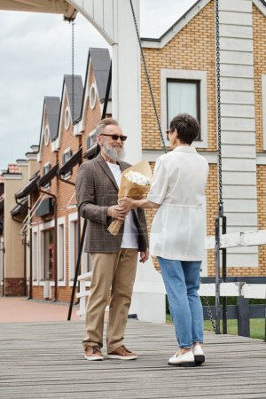 glücklicher älterer Mann mit Bart und Sonnenbrille, der Frau auf der städtischen Straße einen Strauß schenkt, Date, Romanze