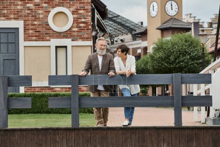 couple âgé heureux, femme regardant l'homme, debout près de la clôture, fond urbain, population vieillissante