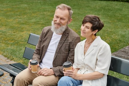 happy elderly man and woman sitting on bench, holding paper cups with coffee, senior couple, romance