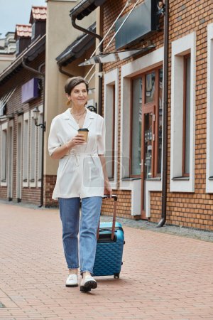glückliche ältere Frau hält Pappbecher in der Hand und geht mit Gepäck, Coffee to go, urbanem Lebensstil