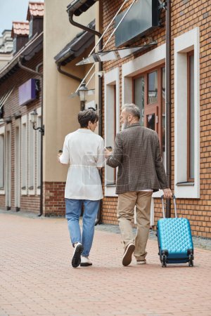 elderly couple, bearded man and woman walking with coffee to go and luggage, urban lifestyle