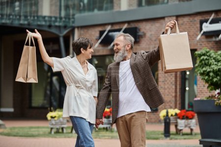 pareja excitada y mayor sosteniendo bolsas de compras, estilo de vida de la ciudad, hombre y mujer feliz, vida anciana