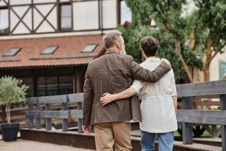 back view of elderly man and woman hugging and walking together outdoors, senior couple, romance