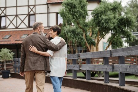 glücklicher und älterer Mann und Frau, die sich umarmen und zusammen im Freien spazieren gehen, älteres Paar, Romantik