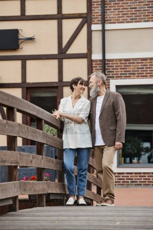 happy bearded man and woman looking at each other, senior couple, standing near bridge, romance