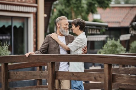 romantic senior couple standing together on wooden bridge and hugging each other, elderly love, bond
