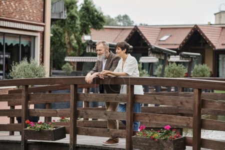 glückliches Seniorenpaar, das zusammen auf Holzbrücke steht, alte Liebe, bärtiger Mann und Frau