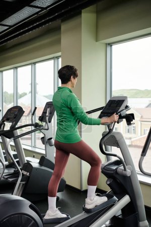 senior activo, mujer de edad avanzada en la ropa deportiva de ejercicio en el gimnasio, utilizando la máquina de ejercicio paso a paso, el deporte