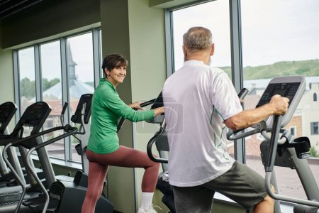seniors activos, mujer feliz mirando al hombre mayor en el gimnasio, ejercitando juntos, pareja de ancianos